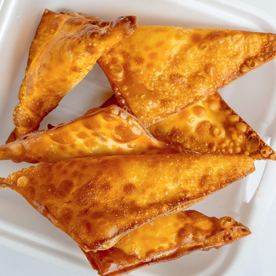 Golden-brown fried wontons, triangular in shape, piled in a white takeout container.